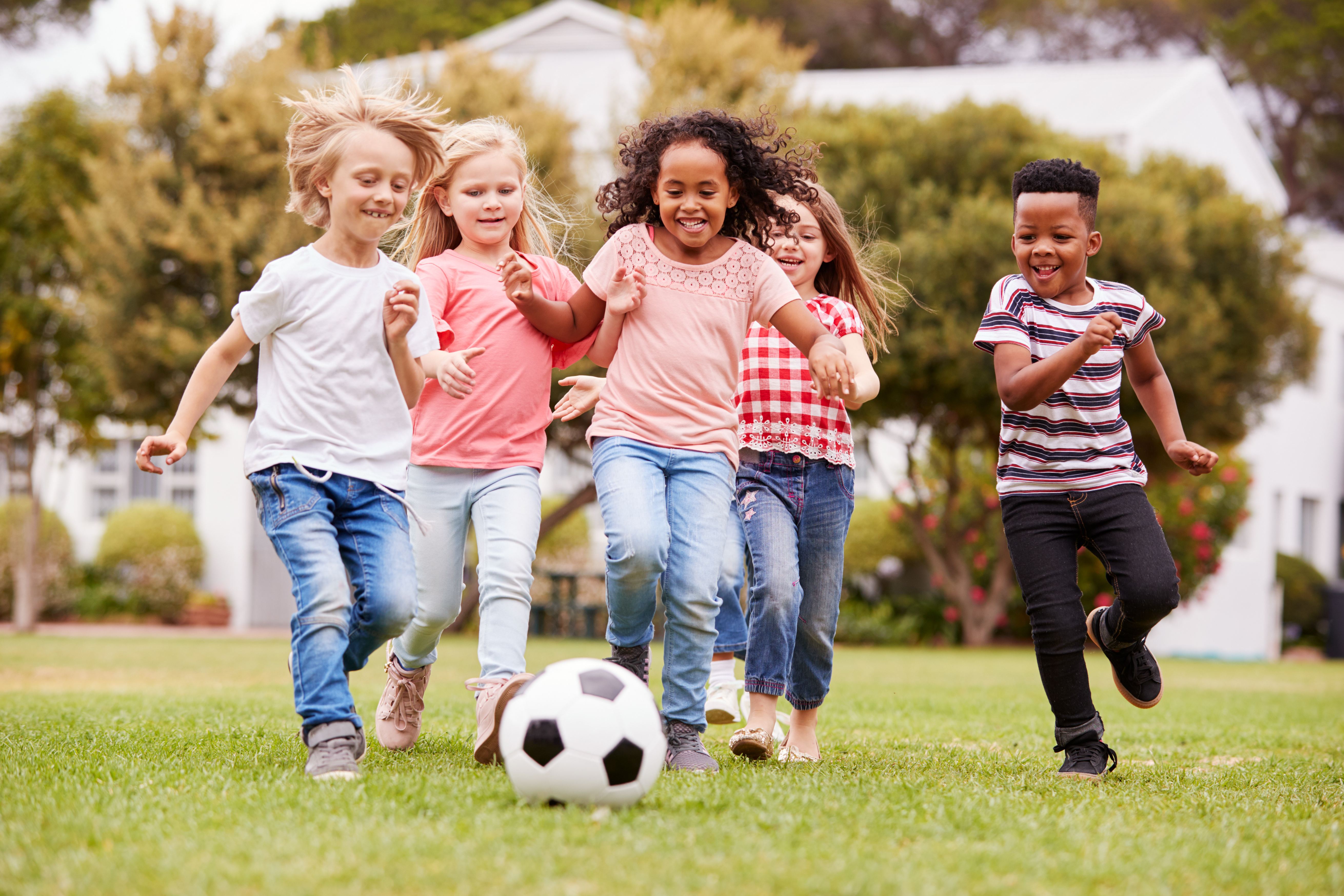 Diverse group of children playing soccer together on a green lawn in a beautiful Bendera housing community, representing joy, belonging, and safe spaces for families
