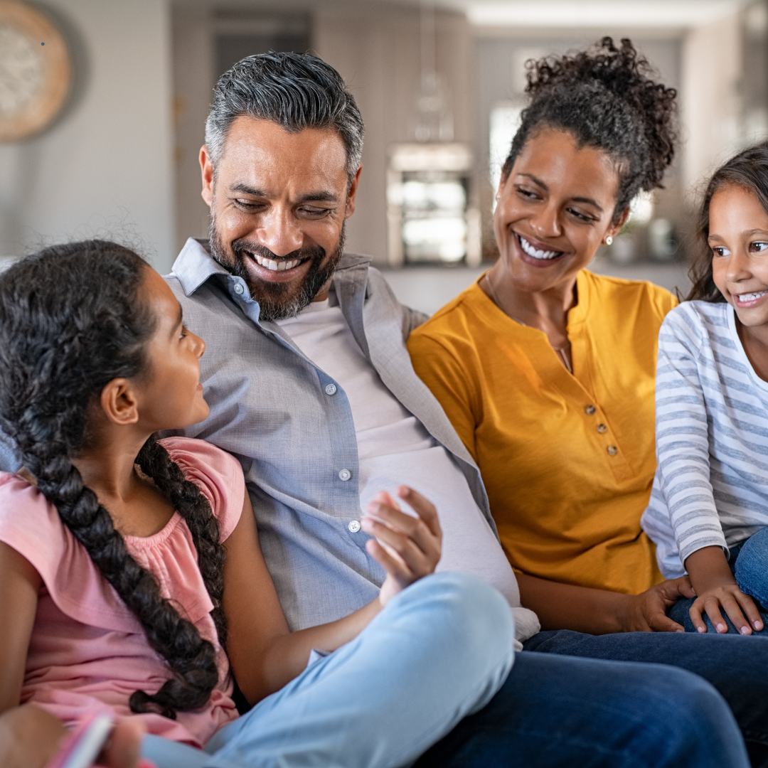 Happy diverse family of four sitting together in their bright, modern home, representing thriving residents in Bendera Housing communities